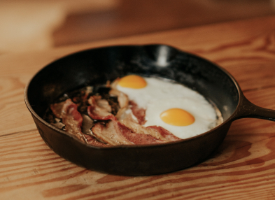 Bacon and eggs cooking in cast iron skillet.