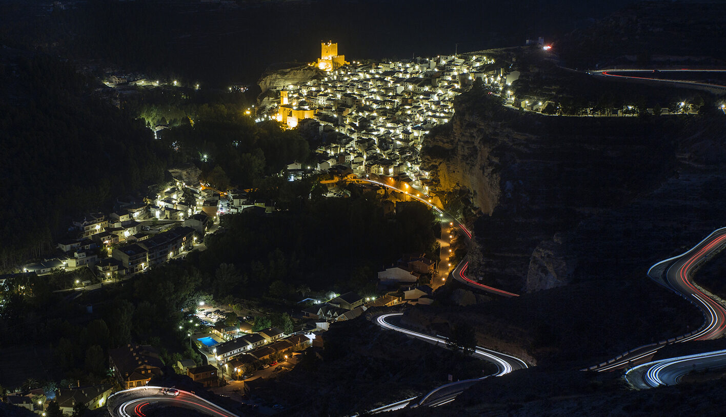 Pueblo iluminado de noche con carreteras serpenteantes.