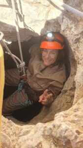 Espeleóloga sonriendo en entrada de cueva con casco.