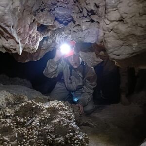 Explorador con linterna en cueva oscura.